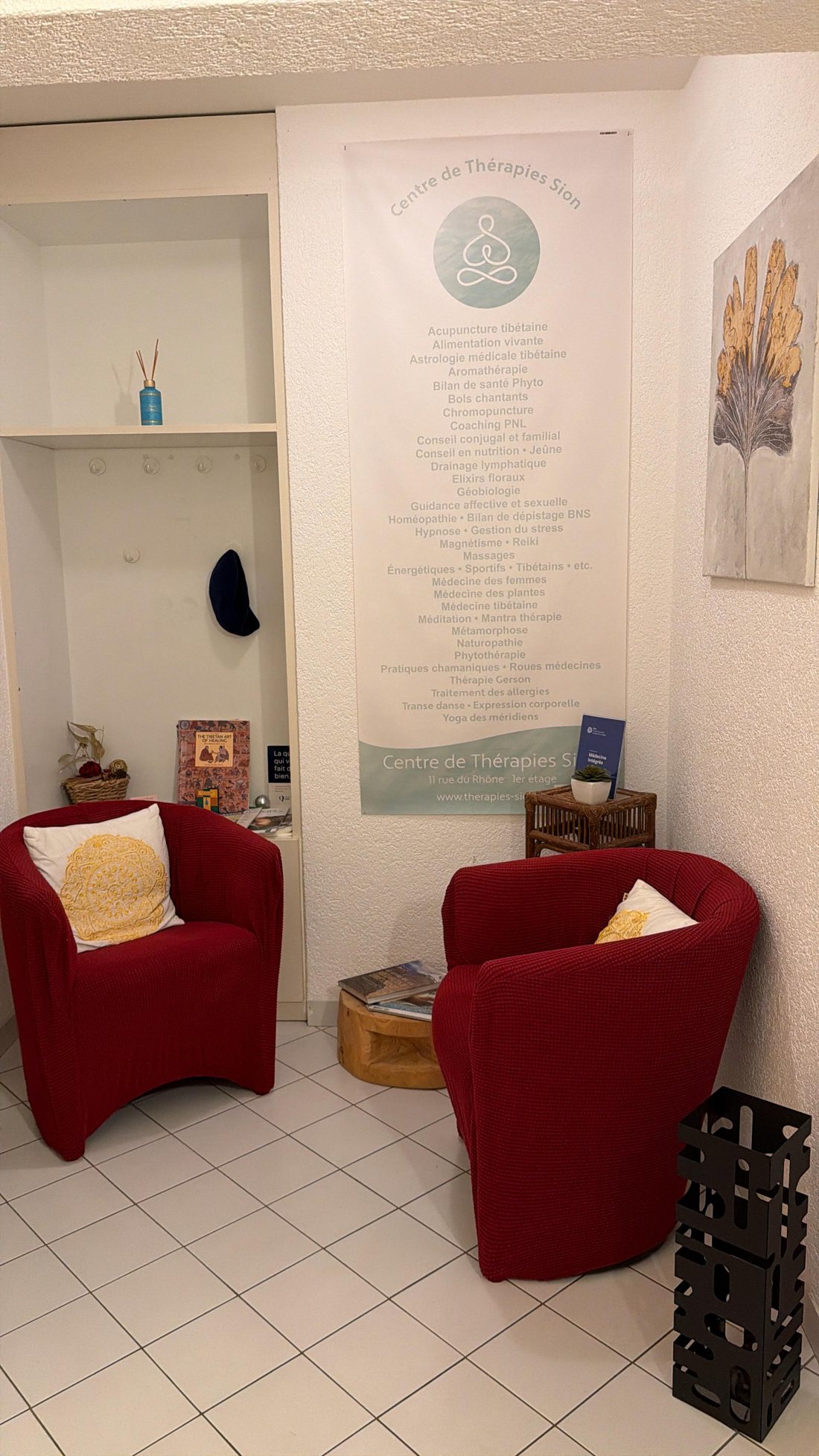 La salle d'attente du Centre de Thérapies à Sion : fauteuils rouges et liste des thérapies proposées